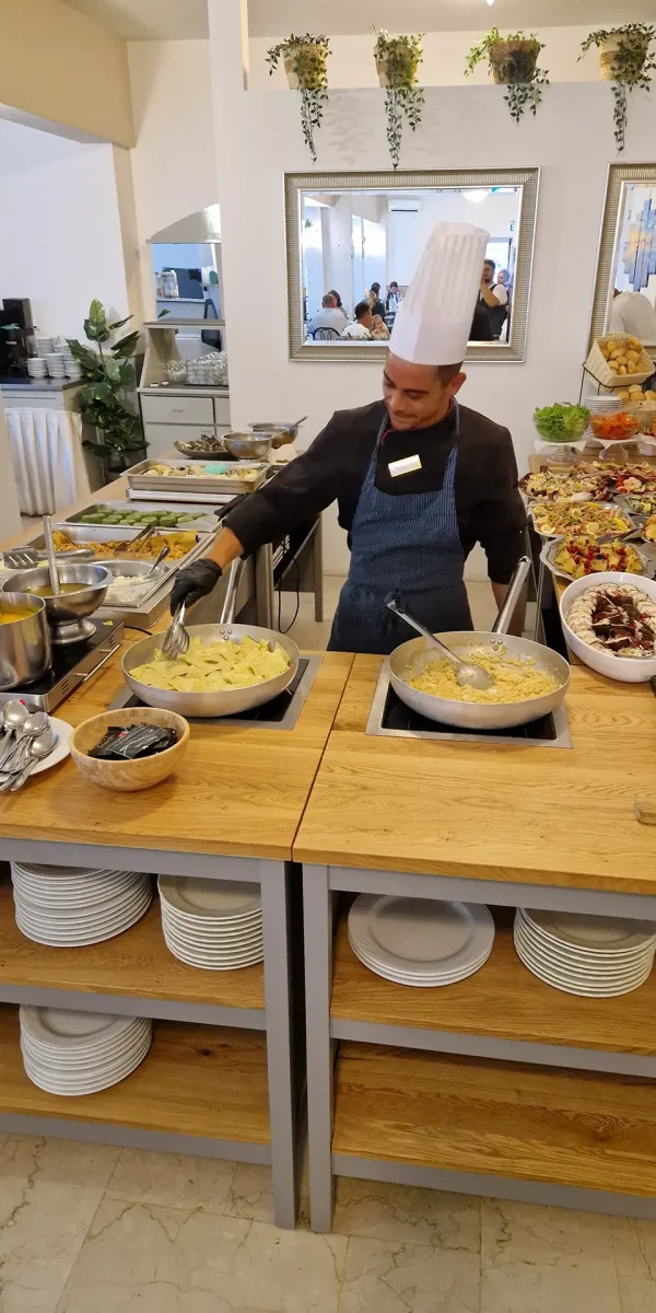 Cuoco che prepara piatti in un buffet ricco di cibo vario.