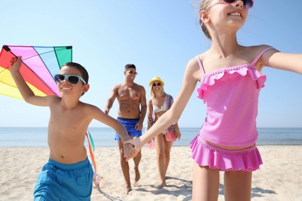 Famiglia felice sulla spiaggia in una giornata di sole, con bambini che giocano con un aquilone colorato.