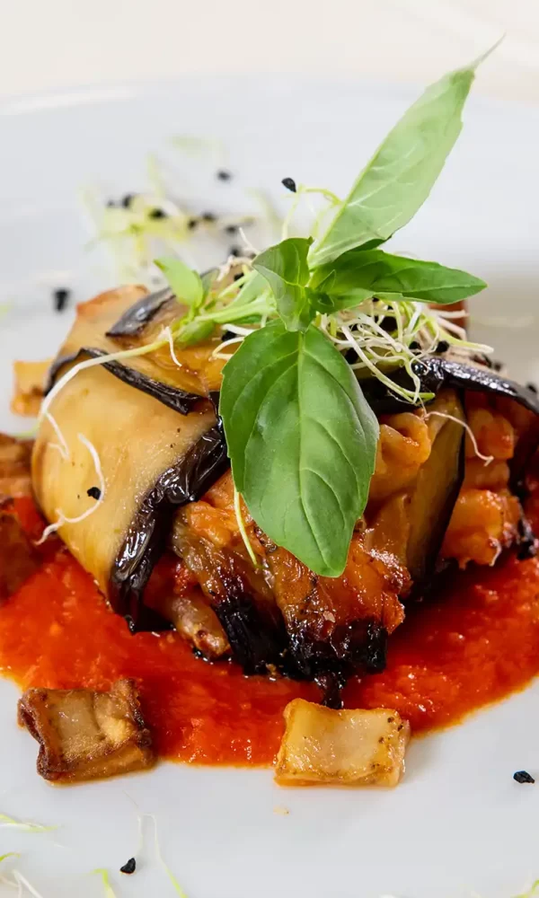 Piatto elegante di parmigiana di melanzane con salsa di pomodoro e guarnizione di basilico.
