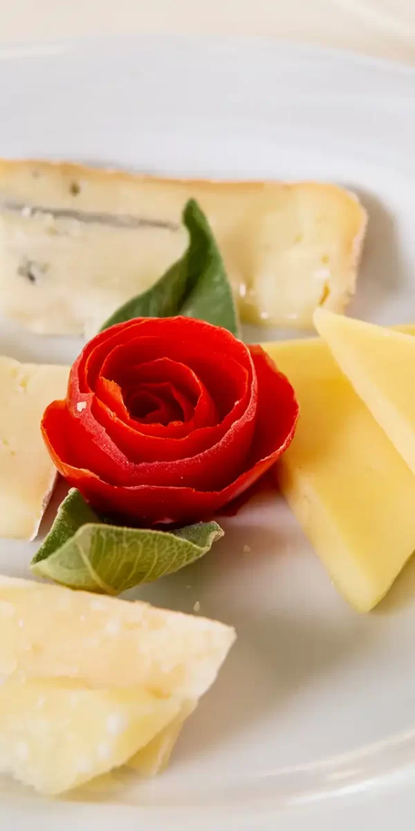 Piatto con varietà di formaggi e decorazione di rosa rossa al centro.
