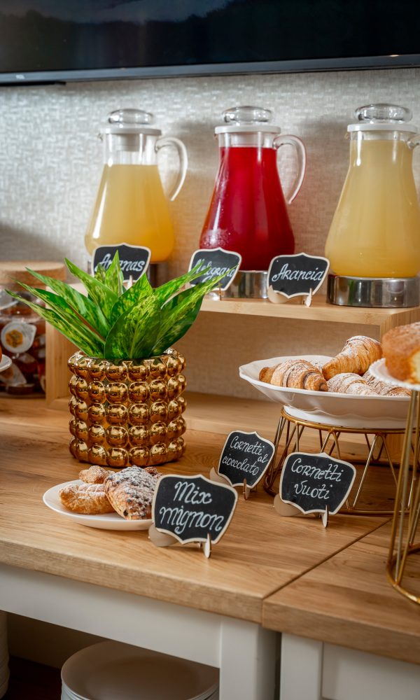 A breakfast buffet with juice jars, pastries, and a plant.