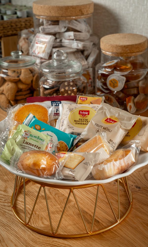 Piatto di snack confezionati su tavolo di legno con barattoli di biscotti sullo sfondo.