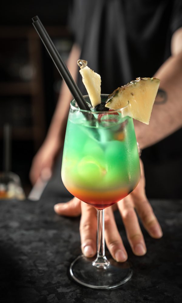 Bicchiere di cocktail colorato con decorazione di ananas e cannucce nere.