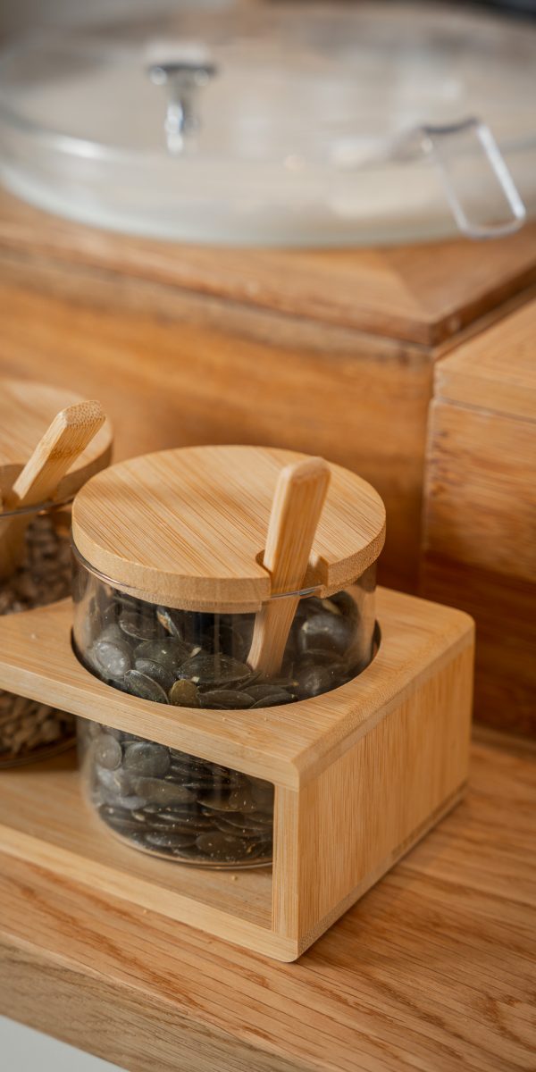 Barattoli di vetro con coperchi di legno contenenti semi su un tavolo di legno.