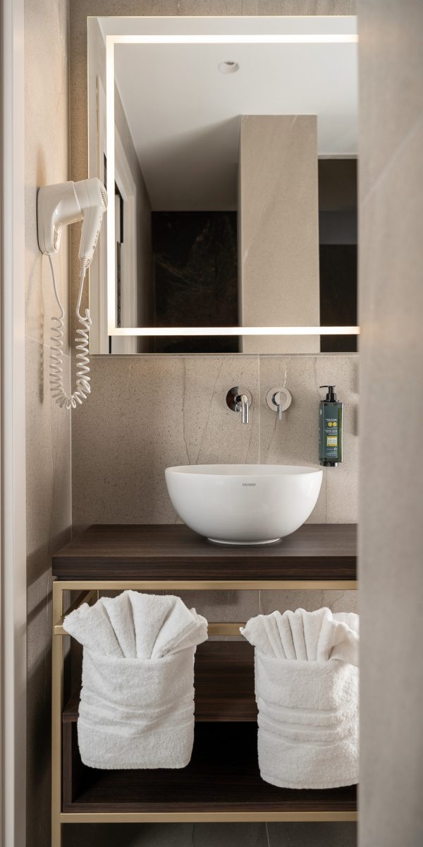 Bagno moderno con lavabo bianco, specchio illuminato e asciugamani arrotolati sotto.