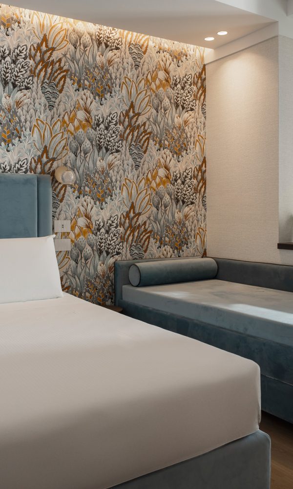 Modern hotel room with a large bed, a chaise lounge, and decorative wallpaper.