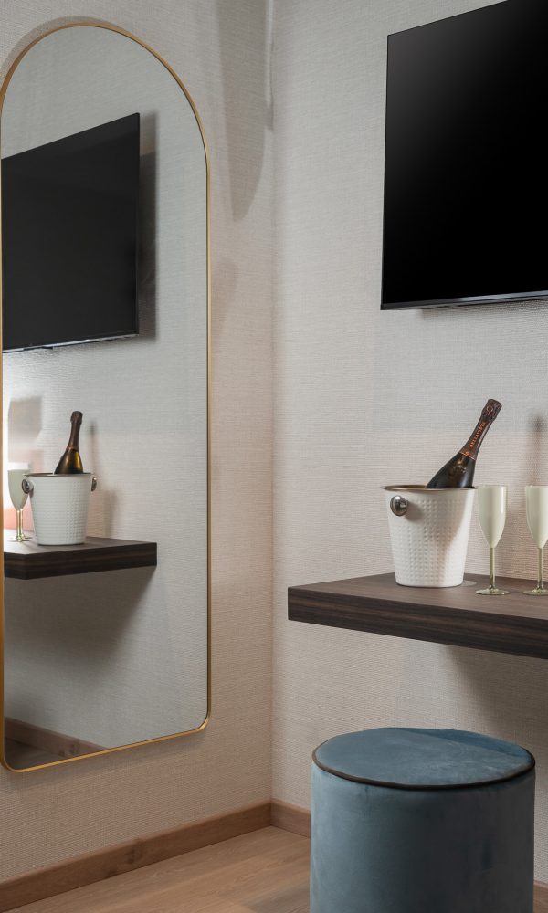 Specchio a parete con cornice dorata, accanto a un tavolino con secchiello e bicchieri di champagne.