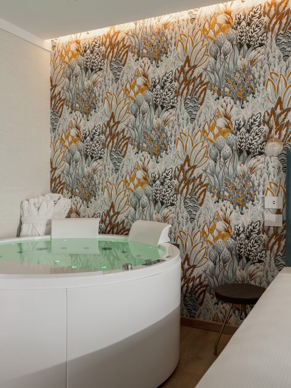 A hotel room with a round jacuzzi tub, a bed, and colorful floral wallpaper.