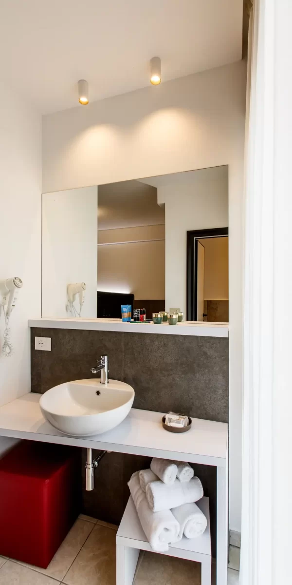 Bagno moderno con lavabo rotondo, asciugacapelli, specchio ampio e asciugamani piegati.