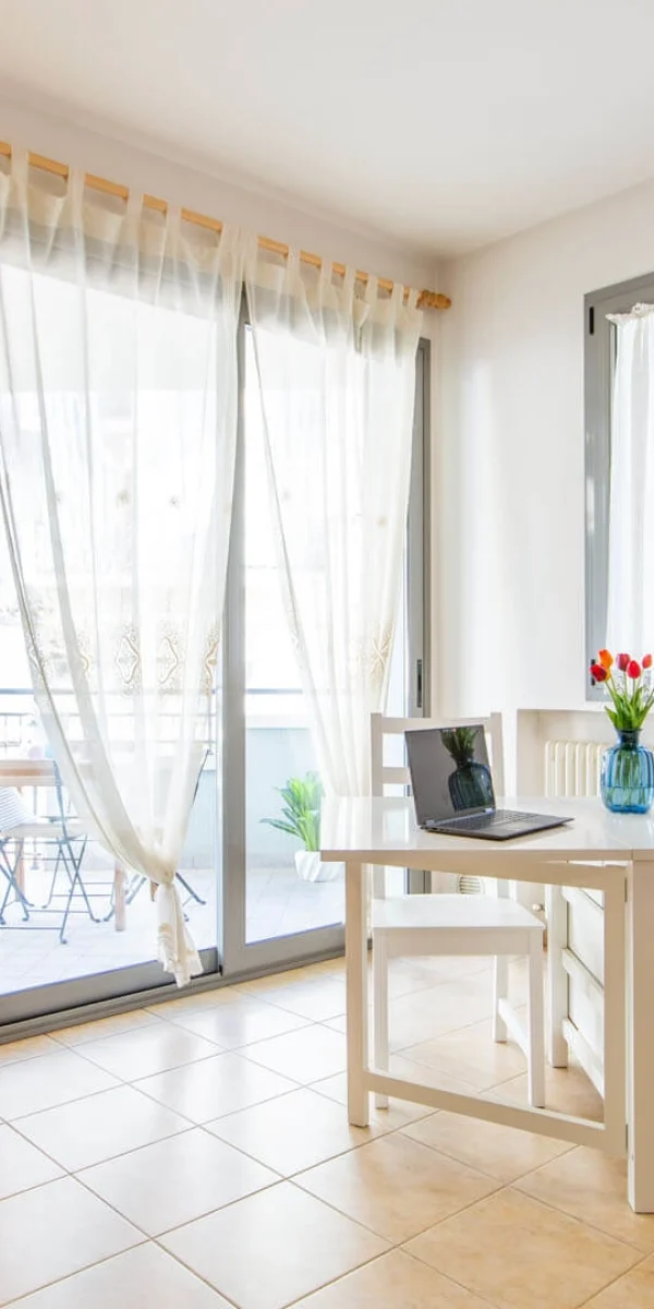 Ein heller Essbereich mit Tisch, Stuhl, Laptop, Blumen in einer Vase und einem Obstkorb.