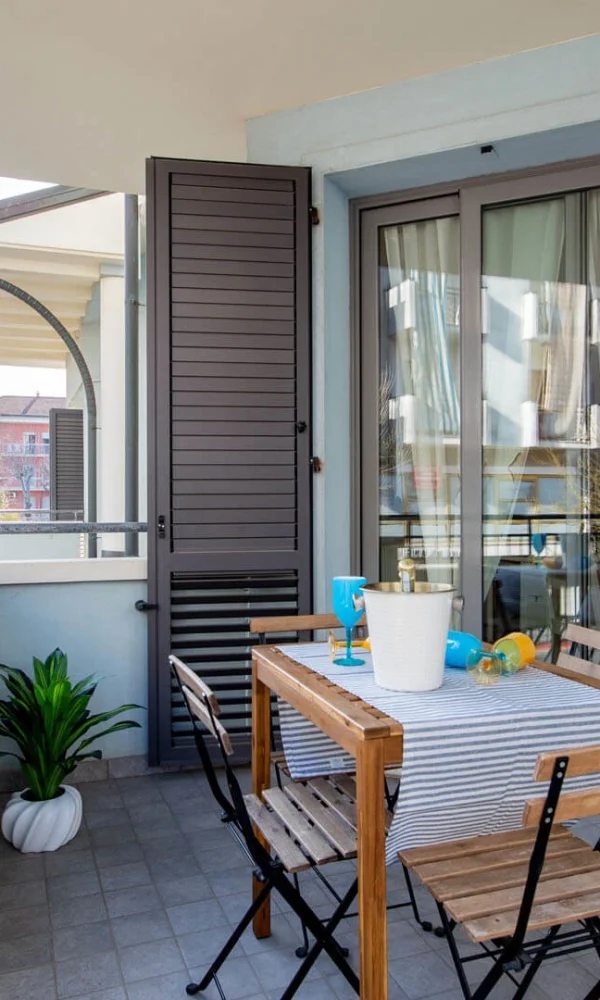 Kleiner Balkon mit Tisch, Stühlen und Pflanzen, der an ein Haus grenzt.