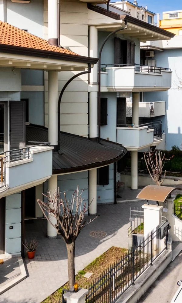 Mehrfamilienhaus mit Balkonen in einer Straße mit geparkten Autos bei sonnigem Wetter.