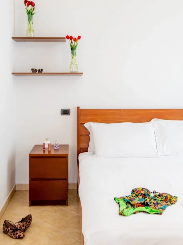 Minimalistisches Schlafzimmer mit Holzmöbeln, Tulpenvasen und Kleidungsstücken auf dem Bett.