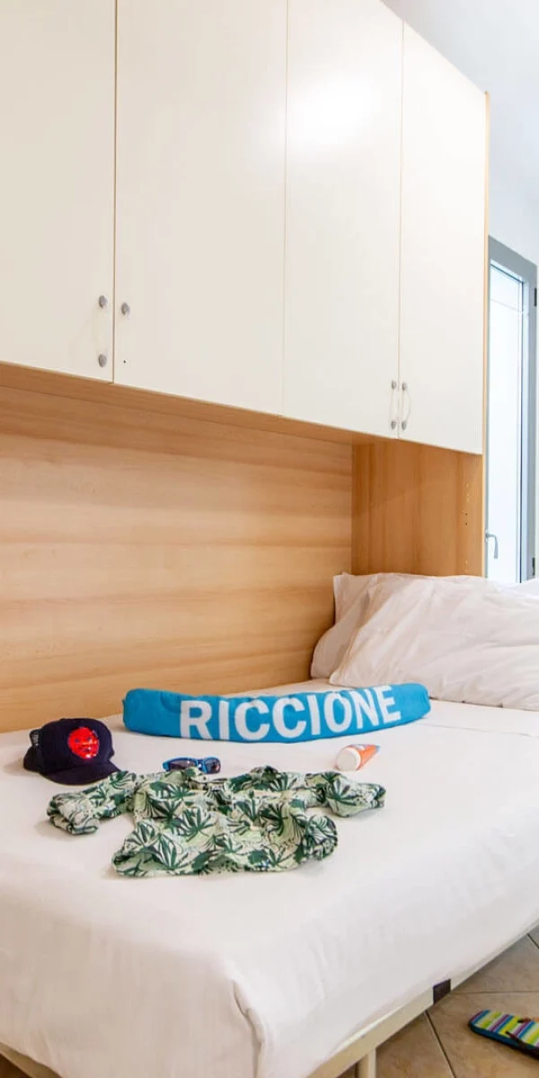 Ein helles Schlafzimmer mit einem Bett, auf dem Kleidung und Accessoires liegen, und einem Stuhl mit Dekoration.