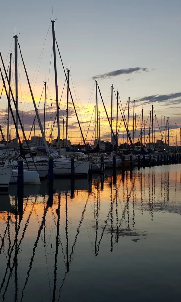 Tramonto su un porto turistico con barche a vela ormeggiate e riflessi sull'acqua.