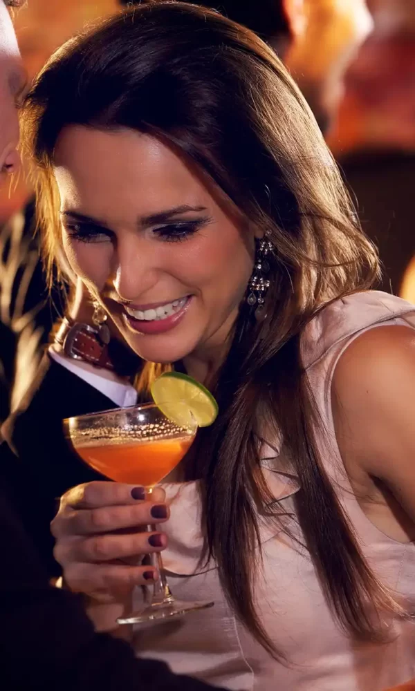 Una coppia sorride mentre conversa e beve cocktail in un ambiente di bar.