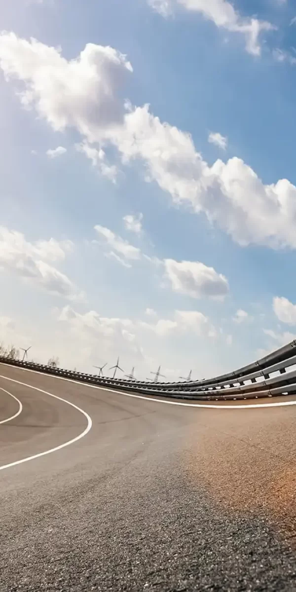 Strada curvilinea con cielo soleggiato e turbine eoliche sullo sfondo.
