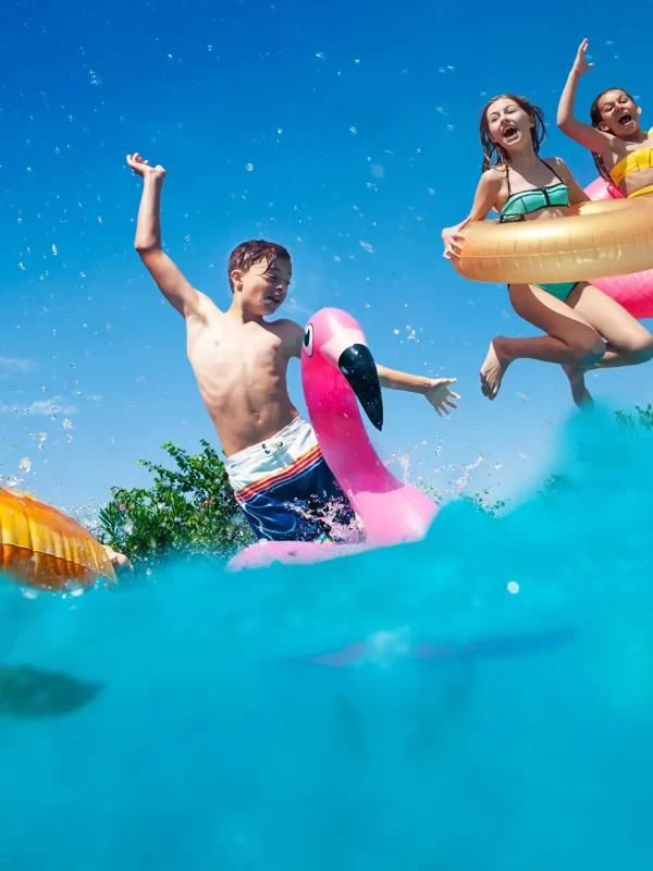 Bambini che si tuffano in piscina con ciambelle gonfiabili colorate.