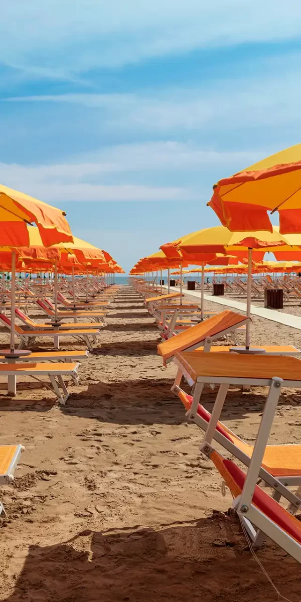 Spiaggia con file di lettini e ombrelloni arancioni.
