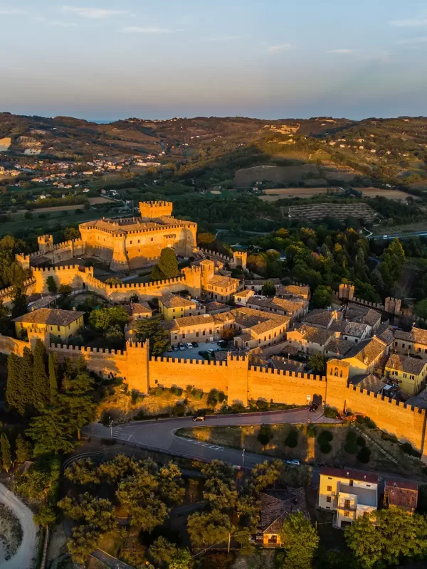 Veduta aerea di un suggestivo castello medievale circondato da mura e colline al tramonto.