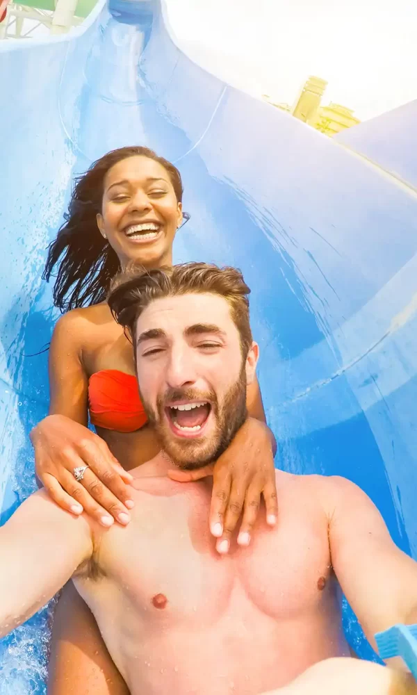 Coppia sorridente si diverte su uno scivolo d'acqua blu.