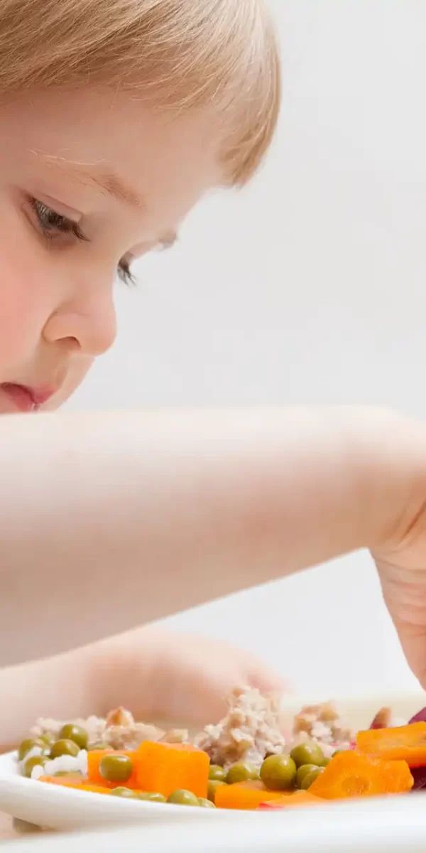 Bambina che mangia verdure colorate da un piatto bianco.