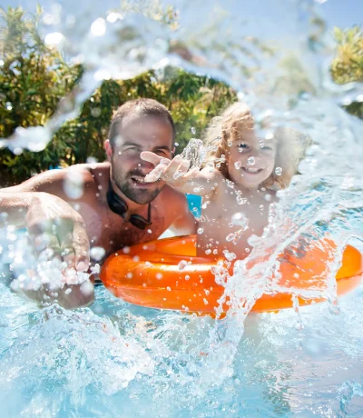Papà e bambino che giocano in piscina con schizzi d'acqua.