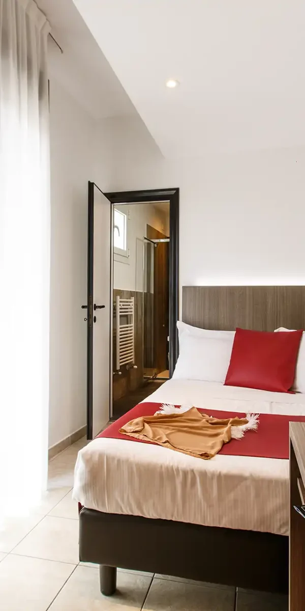 Camera moderna con letto singolo, fiori e laptop su una scrivania.