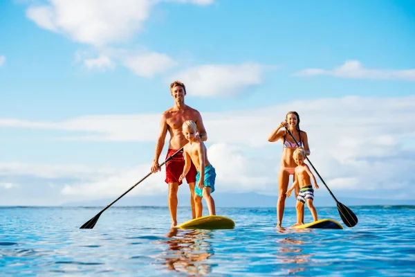 Famiglia che pratica paddleboarding su un mare calmo sotto un cielo sereno.